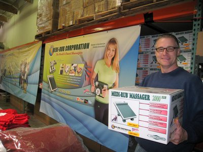 A Man Holding A Box Of Massager Devices In A Warehouse